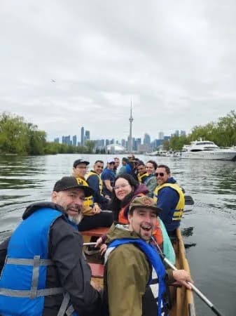 Altrio team members paddling a canoe together with the Toronto skyline behind them