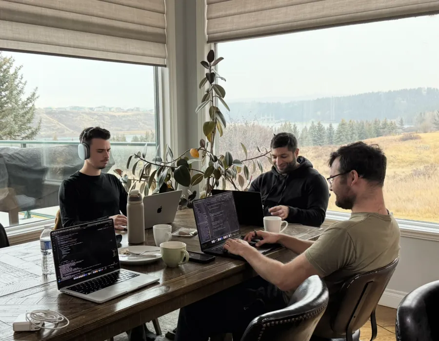 Three Altrio engineers working on laptops around a table, open countryside through the windows behind them