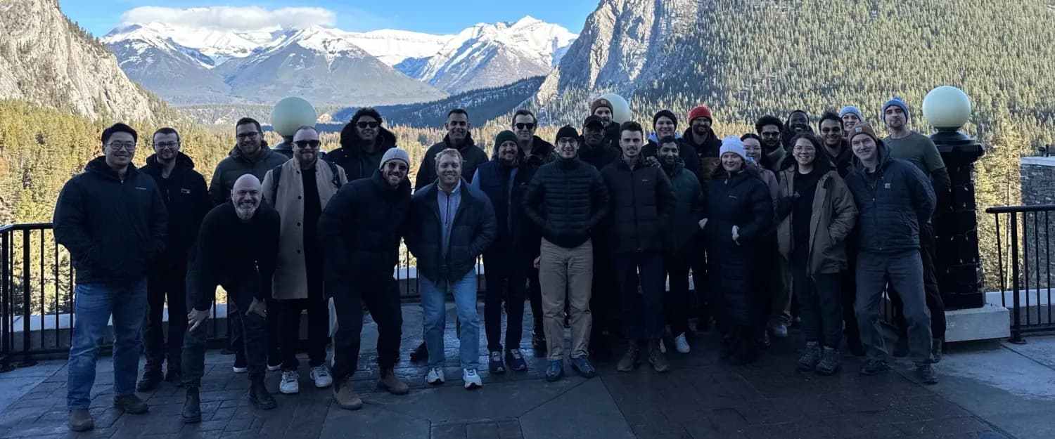 The full Altrio team gathered on a terrace at a company offsite, snow-capped mountains behind them