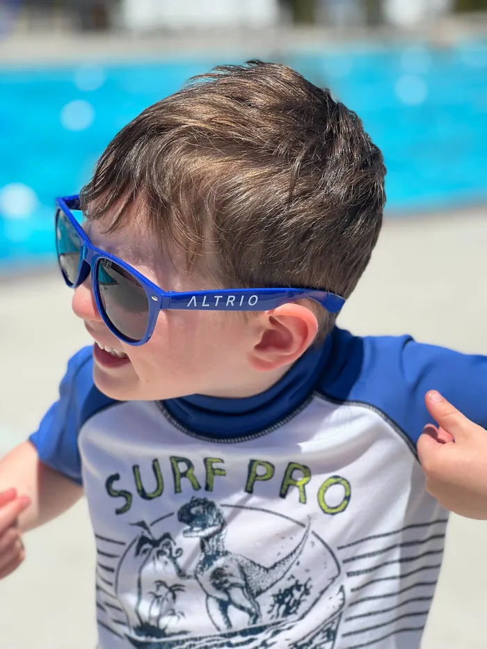 A child grinning poolside in Altrio-branded sunglasses